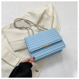 Dettaglio borsa a tracolla trapuntata azzurra con finiture dorate su blazer bianco