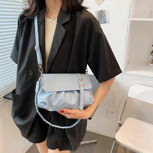 Light blue pleated leather crossbody bag with metal buckle shown on a model in casual setting