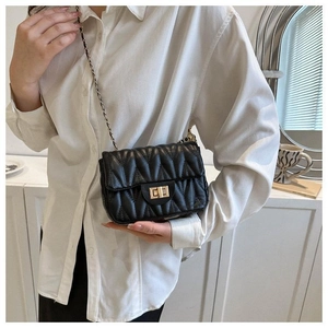 Détail du sac bandoulière matelassé noir avec chaîne dorée porté sur une chemise