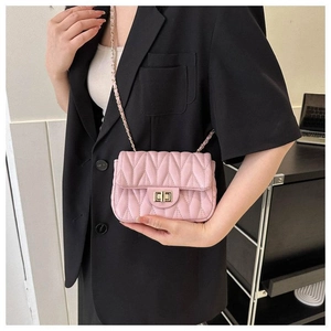 Vue détaillée d'un mini sac bandoulière matelassé rose avec chaîne dorée sur un blazer noir