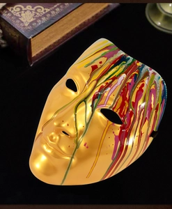 Close-up of golden masquerade mask with colorful paint drips and vintage book background
