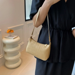 Détail de la texture crocodile beige et fermeture éclair dorée sur un sac baguette chic