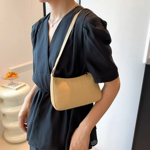 Gros plan d'un sac baguette beige à motif crocodile porté avec une robe noire