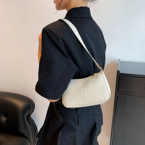 Sac bandoulière blanc à motif crocodile porté par un mannequin en tenue noire chic
