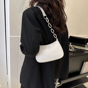 Détail du sac sous l'aisselle blanc à motif crocodile avec chaîne dorée sur l'épaule