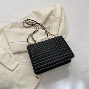 Borsa a tracolla trapuntata nera con catena dorata su sfondo blazer beige neutro