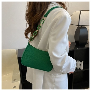 Sac bandoulière vert motif crocodile avec chaîne porté sur une veste de blazer blanc