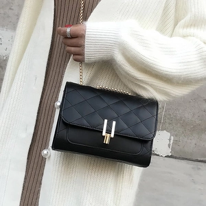 Close-up of black quilted leather crossbody bag with gold chain strap on white cardigan
