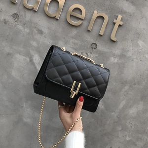 Classic black quilted chain bag with gold rectangular lock shown in hand against wall