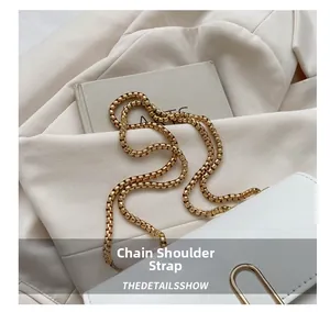 Detail of a white leather crossbody bag featuring a thick gold chain strap on cream fabric