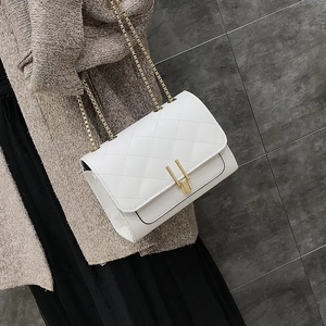 Close-up of white quilted chain bag with gold rectangular buckle on tweed fabric