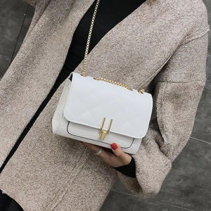 Close-up of white quilted chain bag with gold U-shaped hardware buckle on a beige sweater