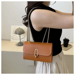 Close-up of caramel brown crossbody bag with gold chain strap and elegant metal buckle