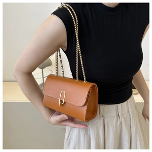 Close-up of brown leather bag with white stitching and gold metal U-shaped clasp detail