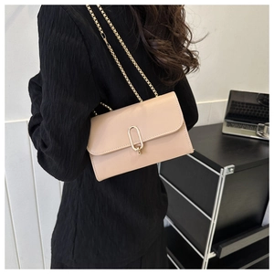 Detail of beige shoulder bag featuring golden chain strap and rectangular metal lock closure