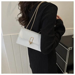 Détail d'un sac carré en cuir verni blanc avec boucle dorée et bandoulière chaîne