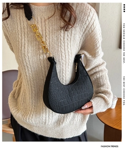 Detail shot of black faux-crocodile leather texture and gold chain on the shoulder bag