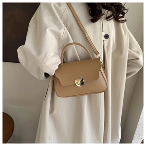 Camel leather crossbody bag with circular gold clasp shown styled on a beige trench coat