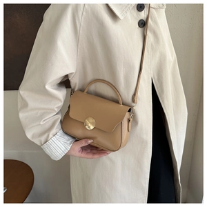 Detail of vintage crossbody bag with gold round buckle and leather strap on trench coat