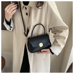 Chic black matte crossbody bag with gold round buckle shown on a model in a beige coat