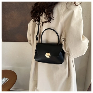 Detail of a black leather handbag with a round gold hardware lock on a model back