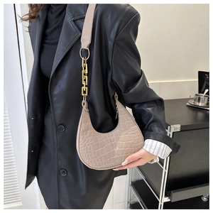Detail of beige crescent underarm bag with crocodile texture and gold chain link strap
