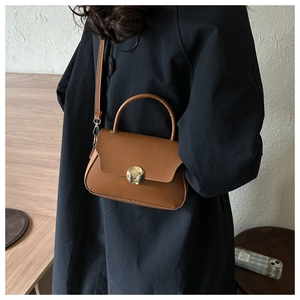 Detail of a brown leather handbag featuring a round gold metal clasp and top handle
