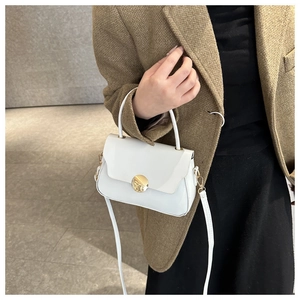 Close-up of a white leather handbag featuring a golden circular clasp and a slim shoulder strap