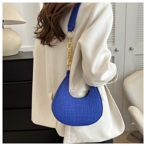 Blue crocodile pattern crescent bag with gold chain strap shown on a white blazer