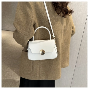 Detail of a white minimalist crossbody bag with golden metal lock worn on a brown wool coat