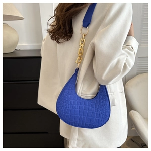 Detail of royal blue crescent underarm bag with gold chain strap on a white blazer