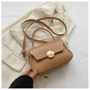 Close-up of caramel leather crossbody bag featuring a large round gold metal buckle