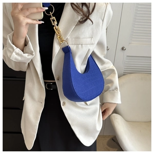 Detail view of blue crocodile pattern hobo bag with thick gold chain worn by a model