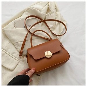 Detail of dark brown leather handbag with gold metal buckle on beige textured fabric