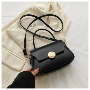 Detail of minimalist black leather crossbody bag with a round gold magnetic clasp