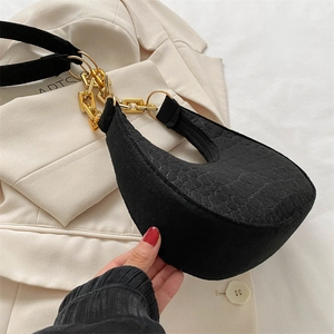 Detail of black crocodile texture hobo bag with a gold metal chain strap on a blazer