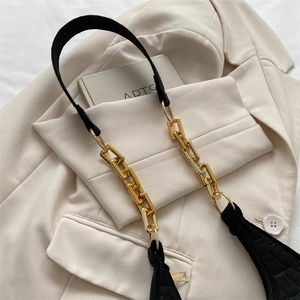 Detail of black embossed crescent bag with chunky gold chain strap on beige blazer