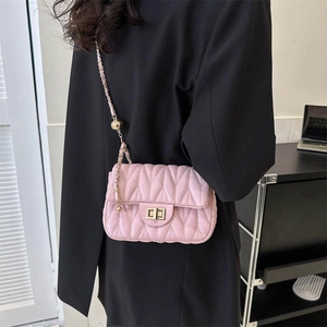 Sac bandoulière rose matelassé chic avec chaîne dorée porté sur un blazer noir