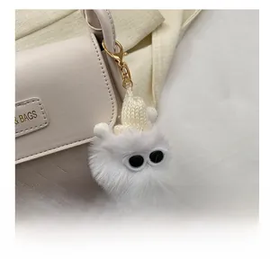 Close-up of a white plush monster bag charm with a knit hat and gold lobster clasp