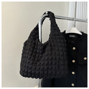 Close-up of black bubble textured tote bag hanging with a tweed jacket on white background