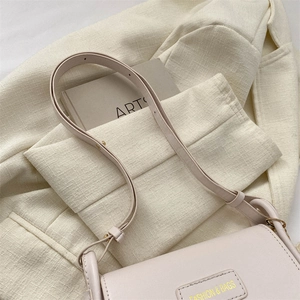Dettaglio della borsa a tracolla in pelle beige chiaro con fibbia e targa dorata