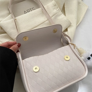 Dettaglio borsa a tracolla beige trapuntata con fibbie magnetiche e pompon di peluche