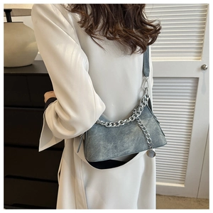 Detail of greyish-blue crossbody bag with silver chain strap on a white blazer model