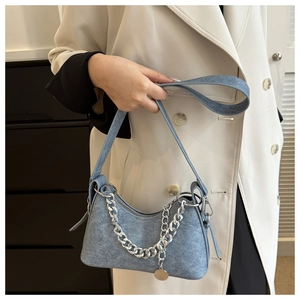 Detail view of light blue denim shoulder bag with silver chain worn on a white coat