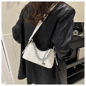 Detail of white leather crossbody bag with silver chains and metallic pendant on a model