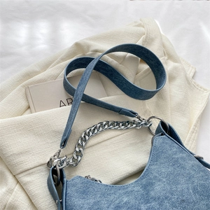 Close-up of blue textured underarm bag with silver chain and long strap on a blazer