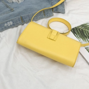 Vista piatta di una borsa a bustina gialla con manico rotondo su denim blu chiaro