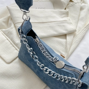 Close-up of blue denim underarm bag with silver chain detail on a white blazer