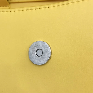 Dettaglio della chiusura magnetica argento con motivo geometrico su borsa gialla