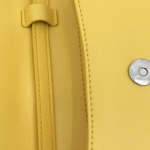 Dettaglio ravvicinato della borsa in pelle gialla con trama liscia e chiusura magnetica